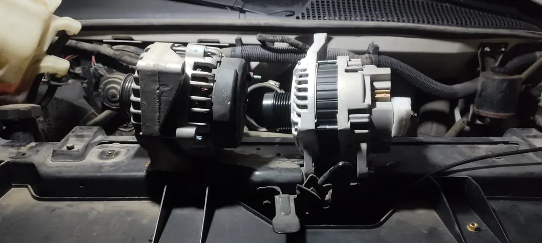 An old alternator and a new one side by side in an engine bay.