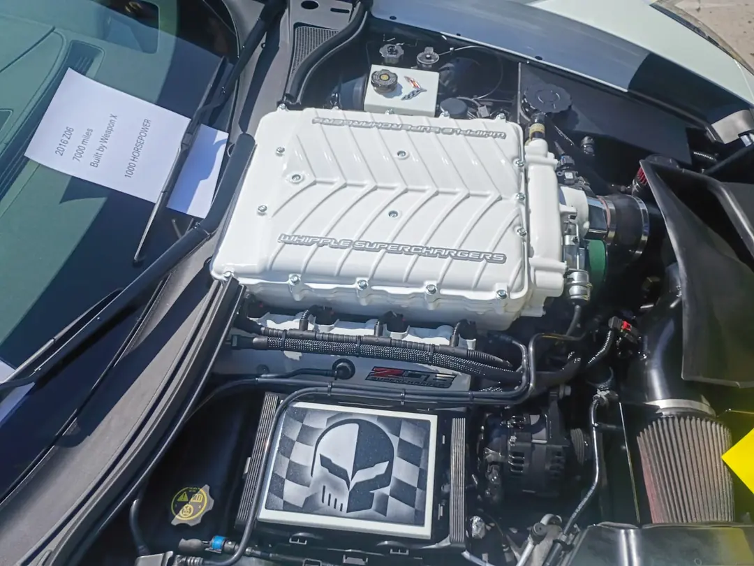 The supercharged V8 engine bay of a Corvette with the hood open.