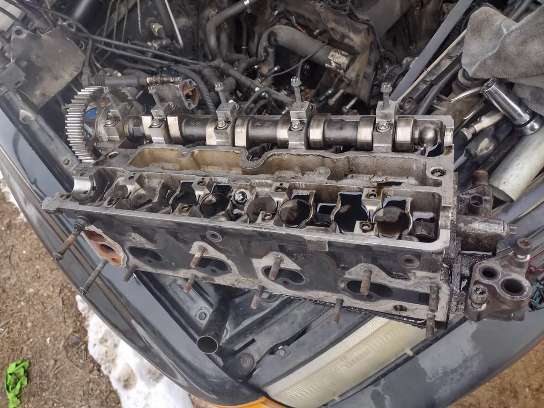 An engine with its cylinder head removed, the head resting on the car and snow on the ground.