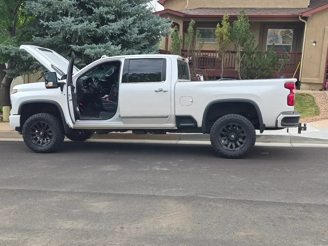 A white Chevrolet Silverado 2500 pickup in a driveway with its hood raised.