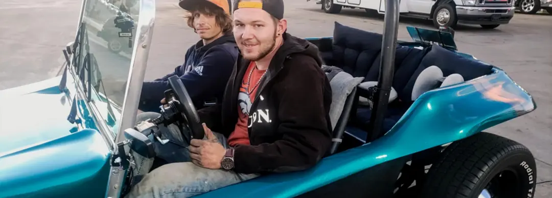 Two men sitting in a teal dune buggy.