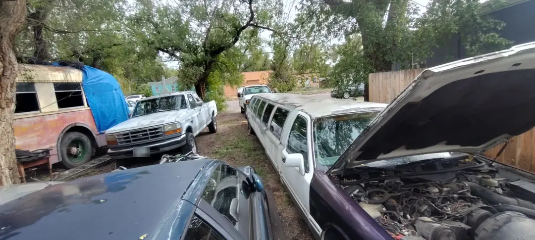 A white stretch limousine with its hood up and engine exposed, parked in a yard beside other vehicles.