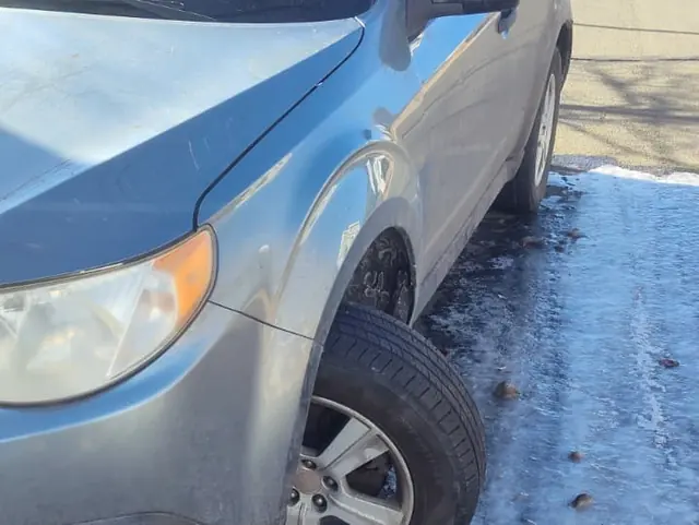 A Subaru Forester at an icy curb, its front wheel sitting at an angle.